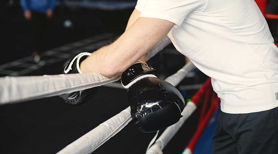 A guy leaning over the ropes with his boxing gloves. It's important to note the quality of gloves when choosing which one to buy.